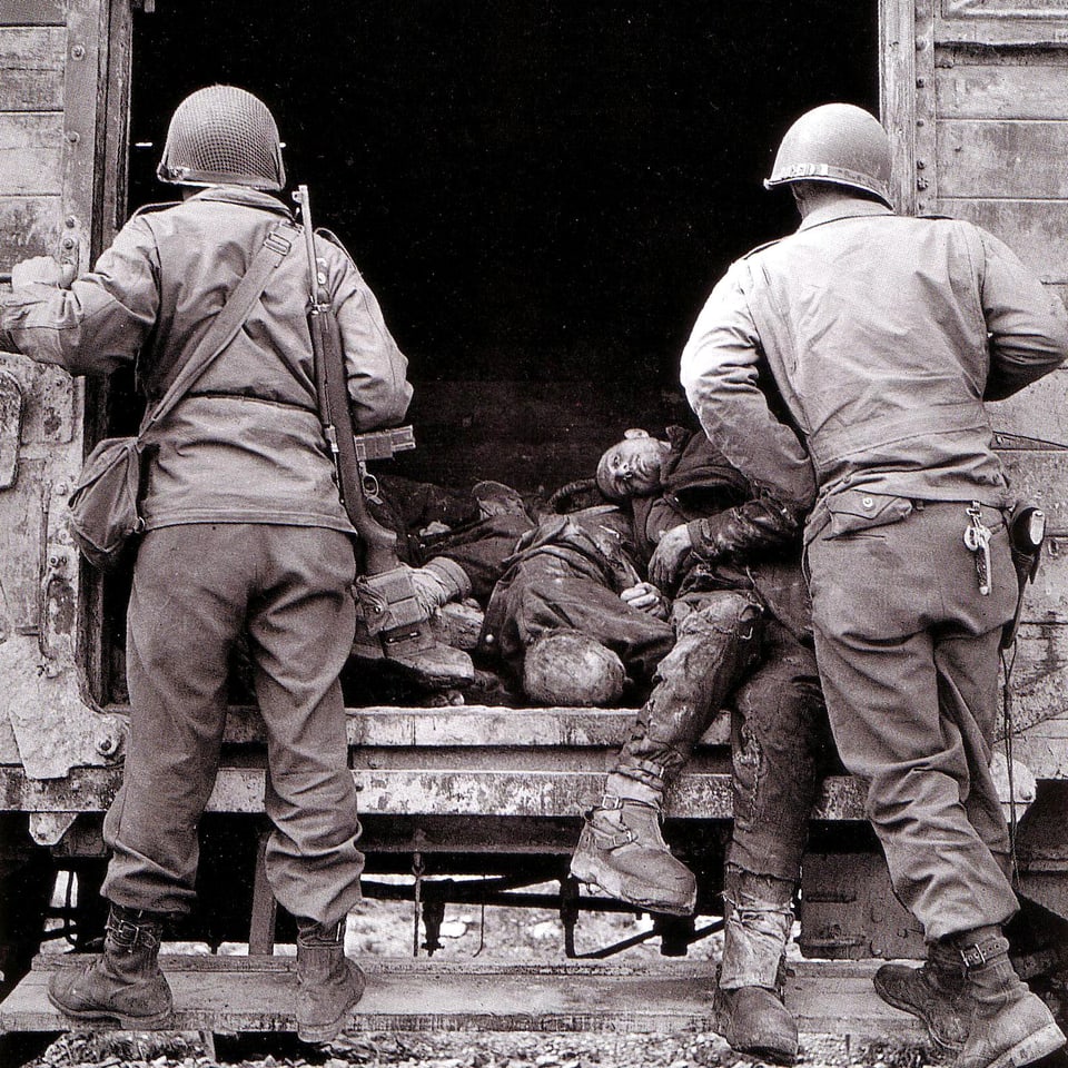 Ein Bahnwagen mit Leichen drin, zwei Soldaten am Wageneingang.
