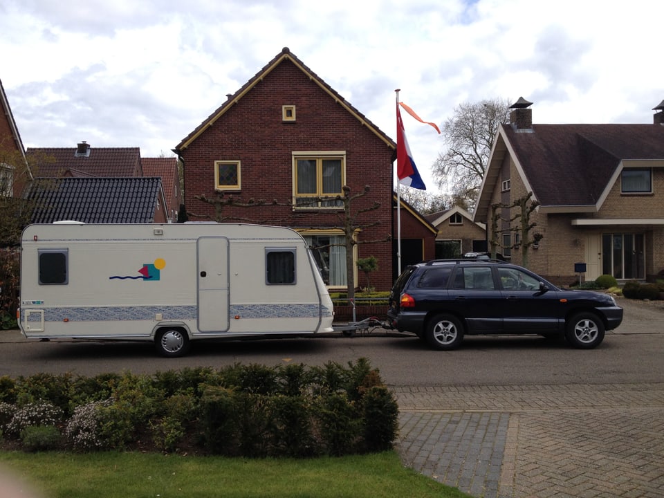 Typisches Holländerhaus, im Vordergrund ein dunkles Auto mit einem grossen Wohnwagen.