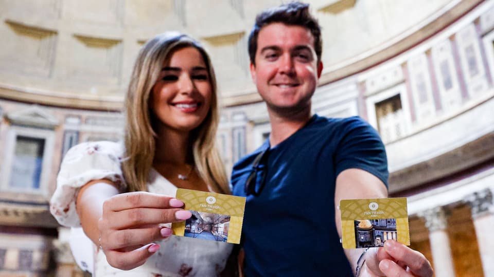 Ein junges Pärchen – Frau und Mann – halten strahlend eine Eintrittskarte in die Kamera.
