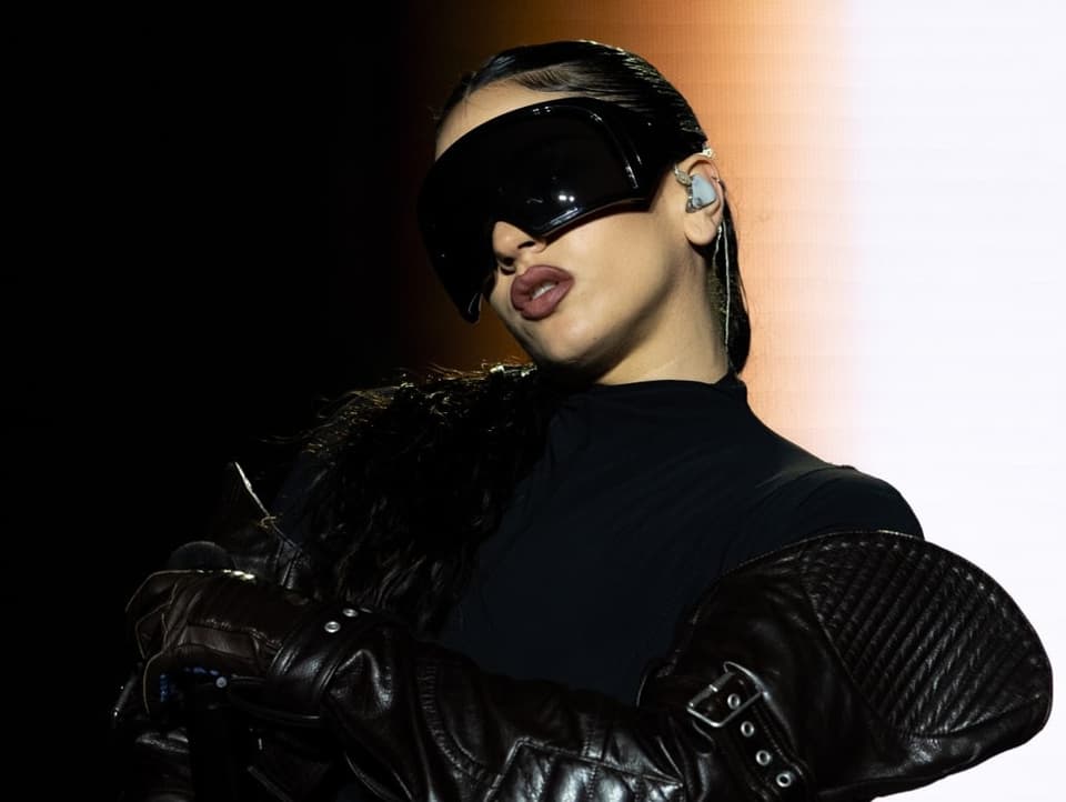 Der Star Rosalía steht in ganz schwarzer Kleidung und einer grossen schwarzen Brille auf der Bühne.