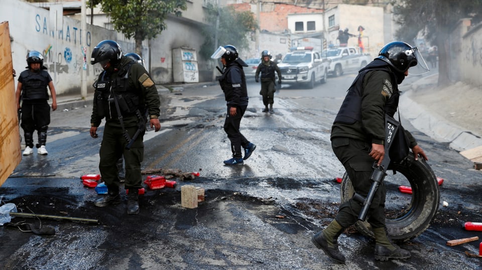 Polizisten in Kampfmontur räumen abgebrannte Barrikaden weg.