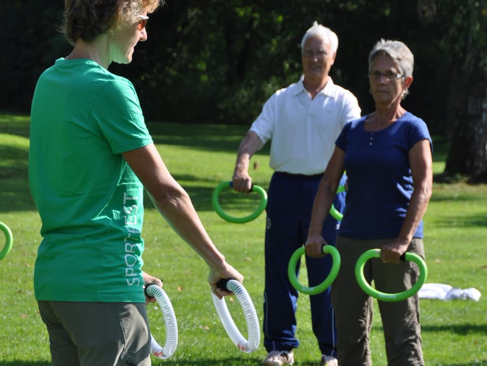 Trainerin hält zwei Ringe in den Händen und zeigt den Teilnehmern Übung vor.