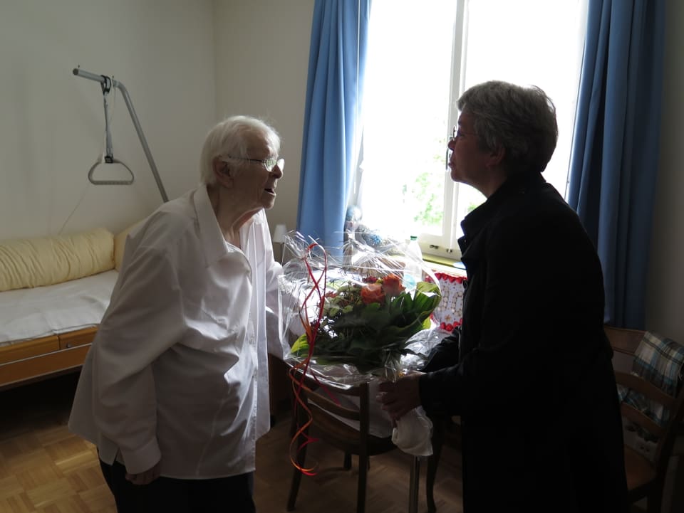 Altherr überreicht einer älteren Dame im Altersheim einen Blumenstrauss