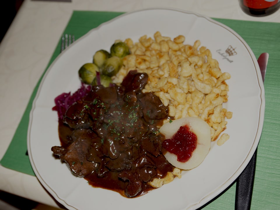 Ein Teller mit Fleisch, Spätzli und Gemüse auf einem Tischgedeck.
