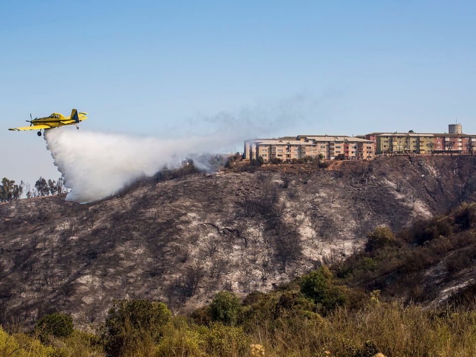 Löschflugzeug löscht ein Feuer nahe einer Siedlung
