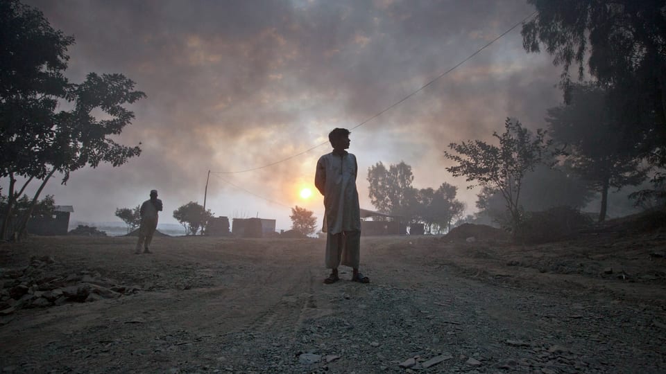 Zwei Männer stehen auf einer Strasse in der Provinz Khyber-Pakhtunkhwa. Dicke Rauschwaden bedecken den Himmel nach einem Angriff im Oktober 2010. (reuters)