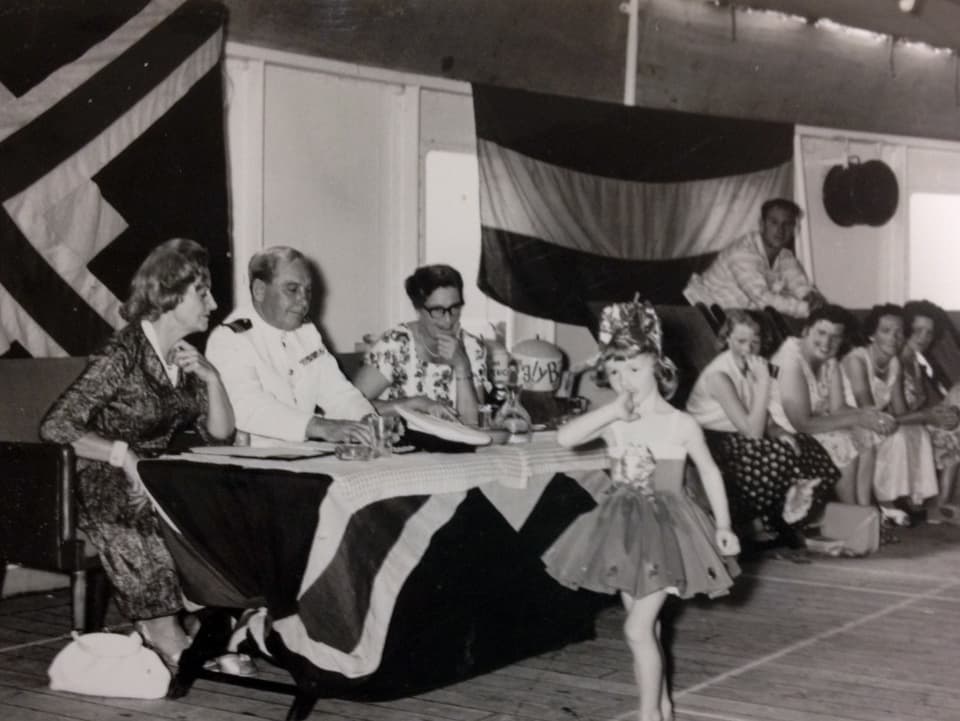 Ein kleine kostümiertes Mädchen spaziert an einem Tisch vorbei, an dem eine Jury sitzt.