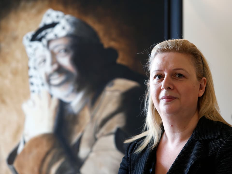 Eine Frau sitzt vor einem Porträt von Jassir Arafat.