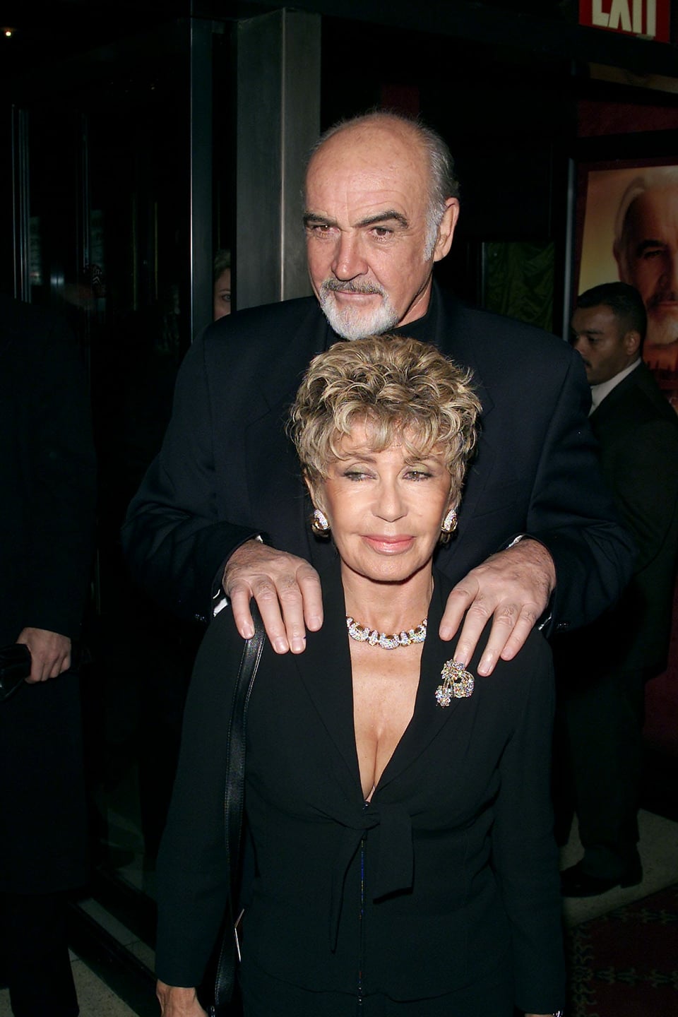 Sean Connery läuft hinter seiner Frau Micheline Roqueburne und hält von hinten ihre Schultern, während sie beide laufen.
