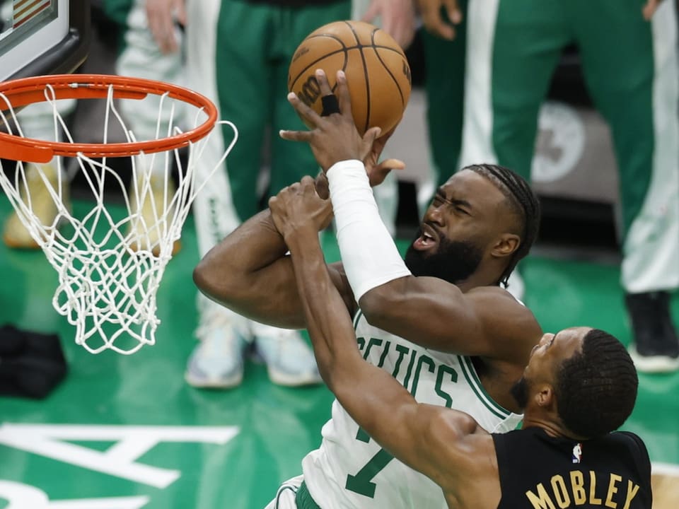 Zwei Basketballspieler, einer in grüner und einer in schwarzer Kleidung, kämpfen um den Basketball am Korb.