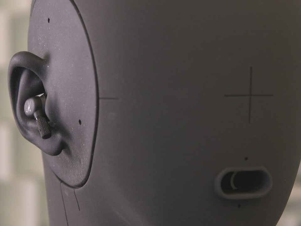 Ein graues Kunstkopf zum Testen von Kopfhörern mit In-Ear-Kopfhörern in den Ohren.