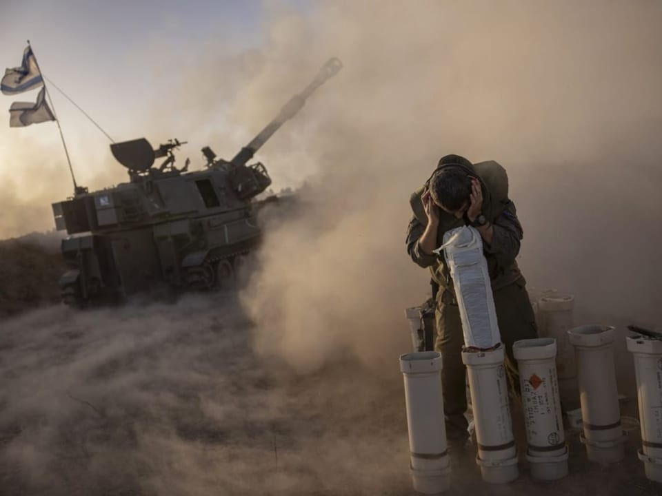 Soldat kniet neben Munition vor einem Panzer in staubiger Umgebung.