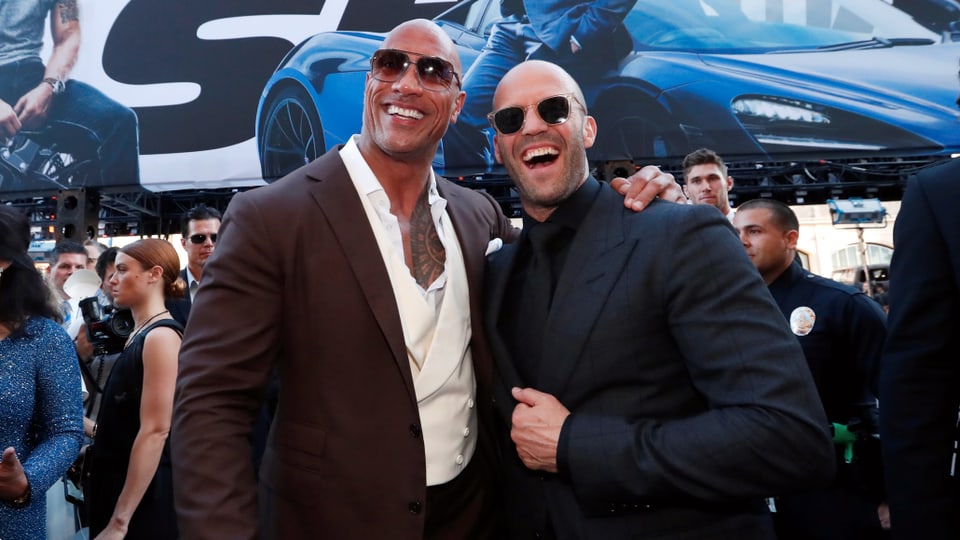 Dwayne Johnson und Jason Statham lachen in die Kamera und tragen beide Sonnenbrillen.