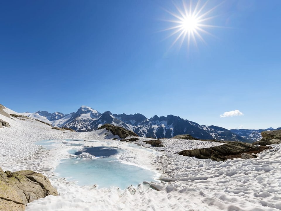 Wolkenloser stahlblauer Himmel mit Sonne rechts, unten Gebirge mit Schneeresten