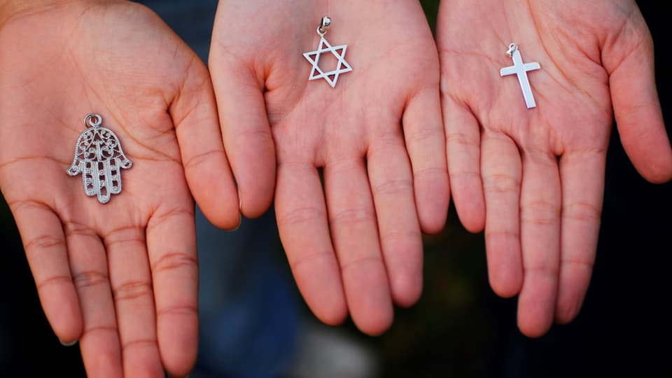 Drei hände halten jeweils ein religiöses Symbol: eine Hand der Fatima, einen Judenstern, ein Kreuz.