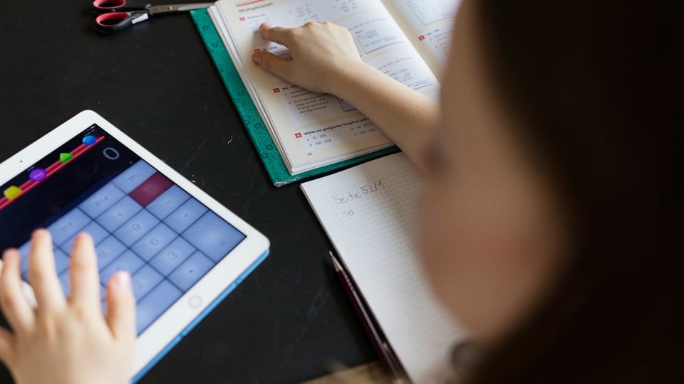 Ein Mädchen arbeitet mit einem Tablet und einem Buch.