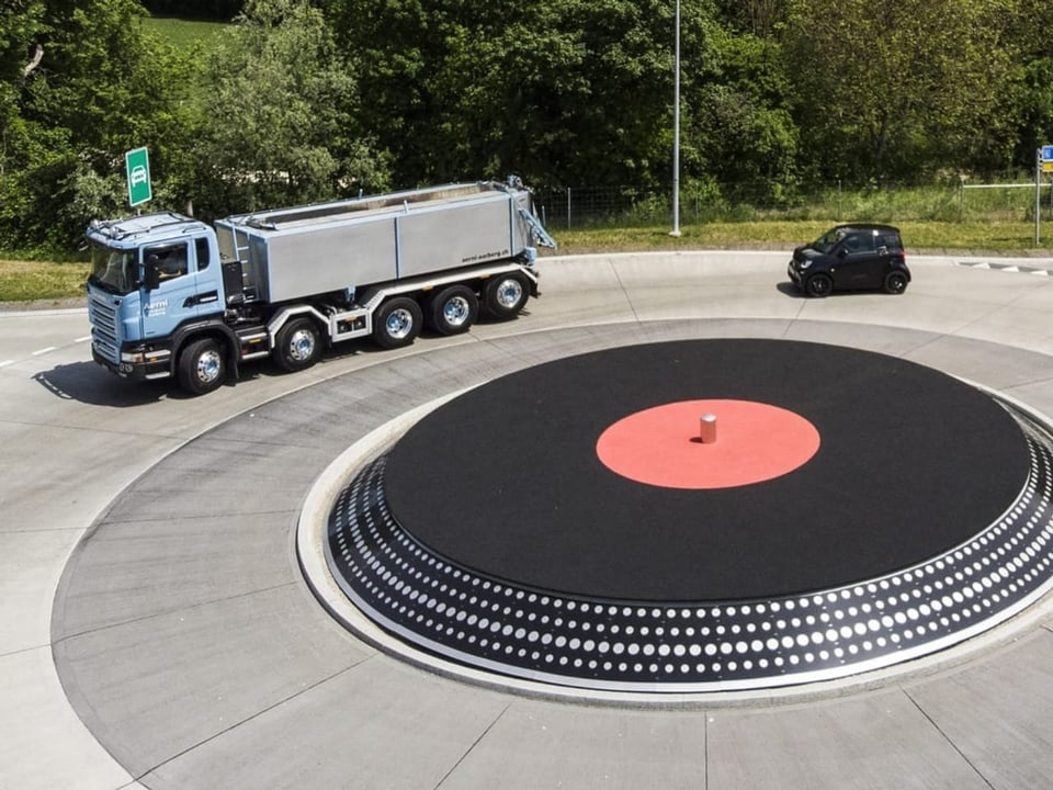 Lastwagen und Auto fahren um einen Kreisel in Form eines Plattenspielers