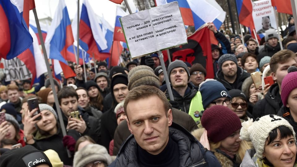 Hinter Nawalny stehen viele Leute mit Plakaten und russischen Fahnen.