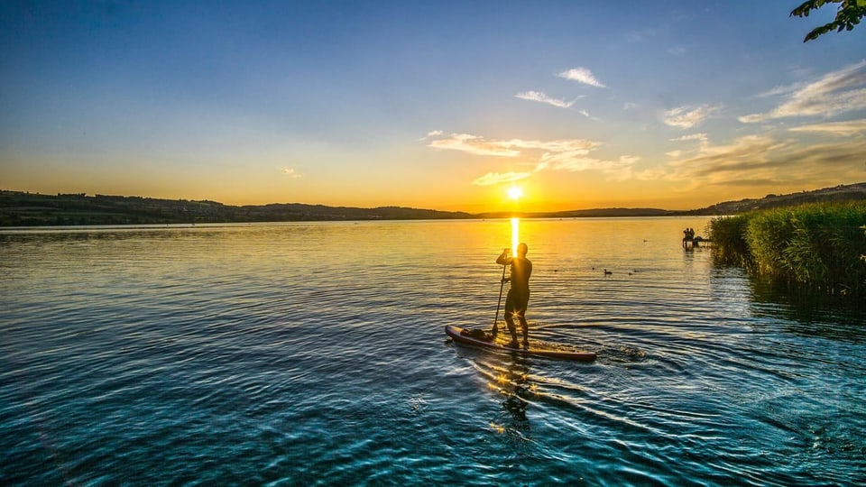 Sonnenuntergang am See, Stand Up Paddler im Vordergrund. 