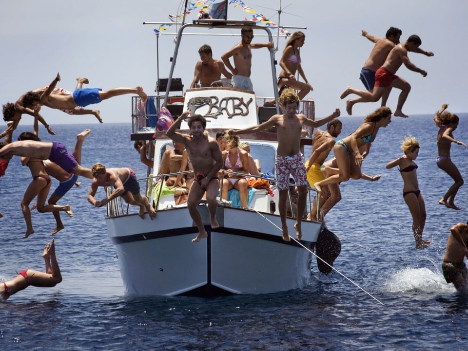 Junge Menschen springen von einem Boot ins Meer.