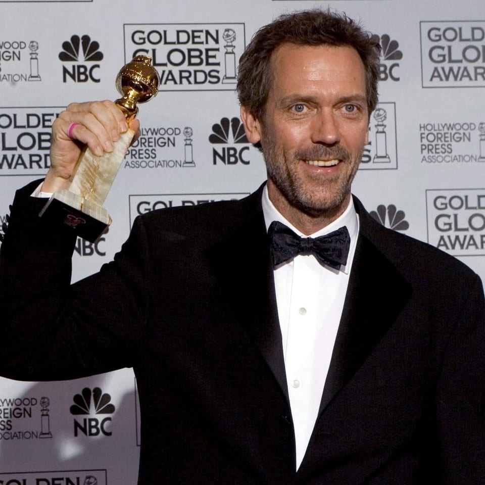 Hugh Laurie im Anzug hält einen Golden Globe - Award in der Hand.