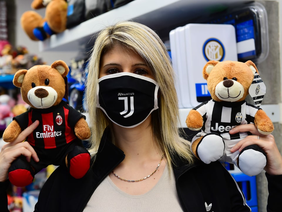 Eine Frau mit Maske hält 2 Stoffbären in den Farben von Juventus und Milan in die Höhe.