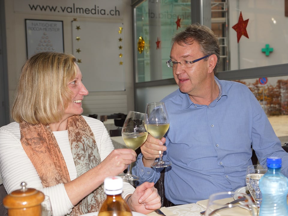 Eine Frau und ein Mann stossen mit einem Glas Weisswein an.