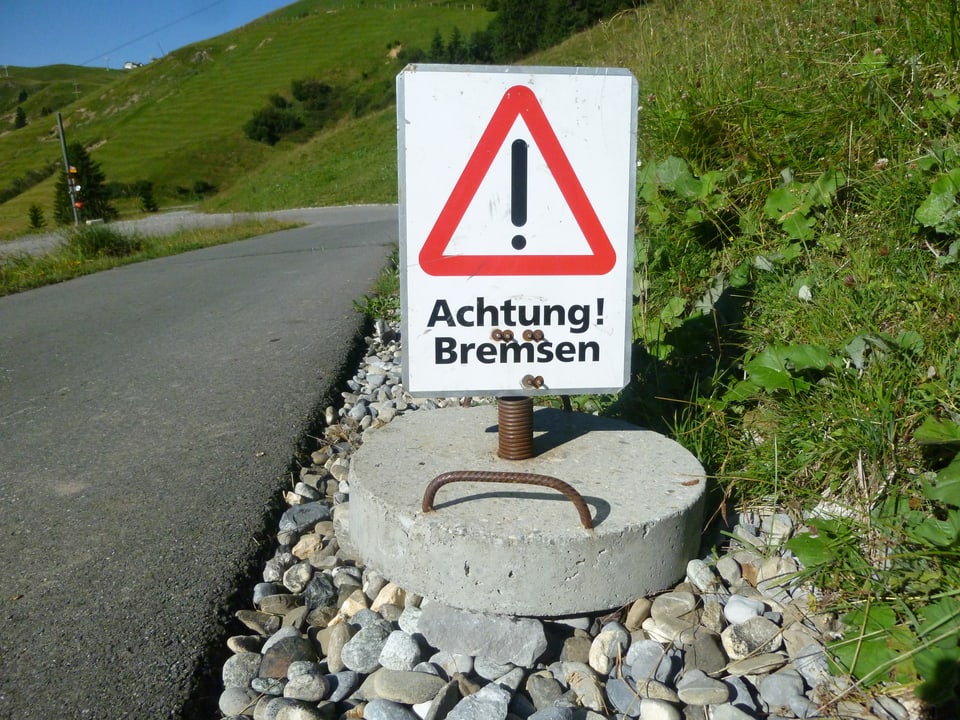 Vor einer Kurve steht eine Warntafel «Achtung Bremsen»