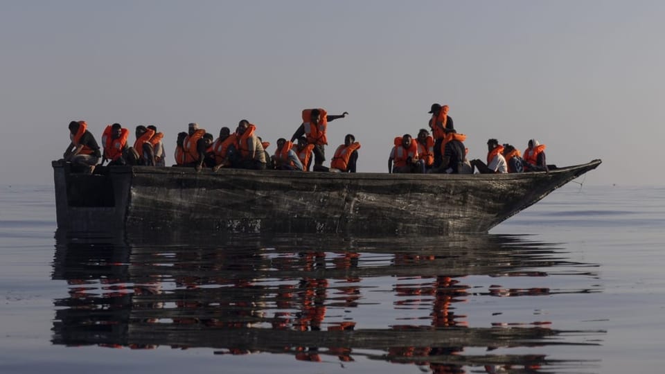 Migranten mit Schwimmwesten sitzen auf einem Rettungsboot.