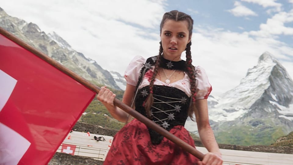 Junge Frau mit Zöpfen, hält Schweizer Fahne, im Hintergrund Berge.