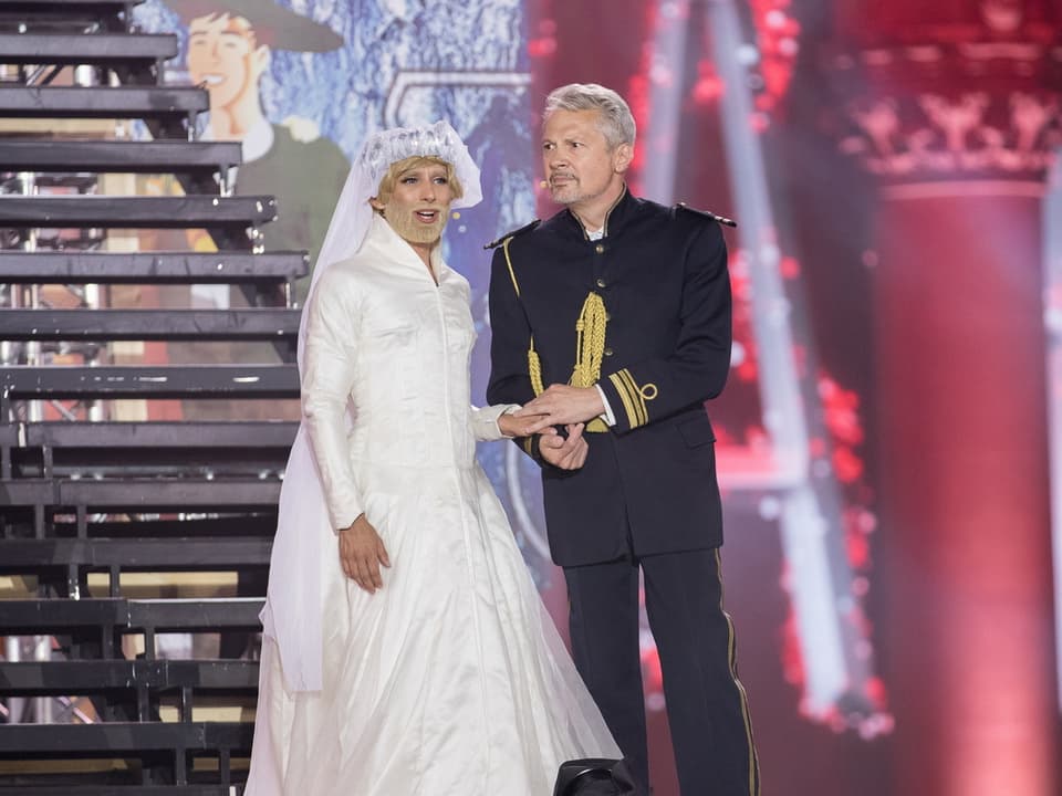 Als Frau gekleideter Mann im Hochzeitskleid mit Mann in Kapitänsuniform auf Bühne