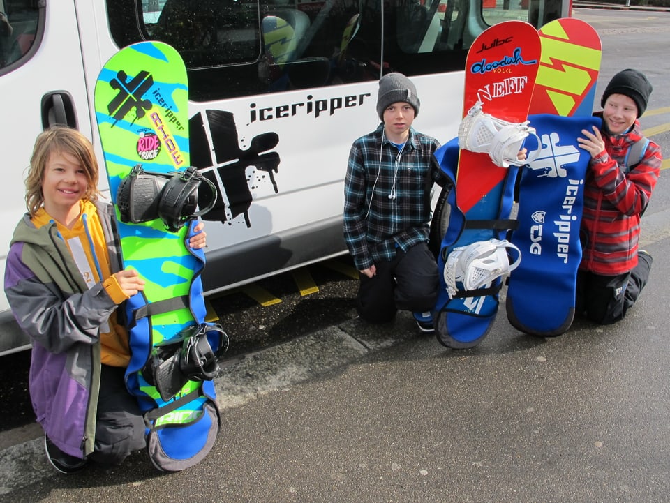 3 Kinder posieren mit Snowboard vor einem Bus