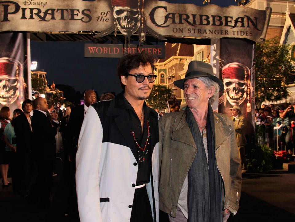 Johnny Depp (links) neben Keith Richards (rechts) vor einem Pirates of the Carribean-Schild