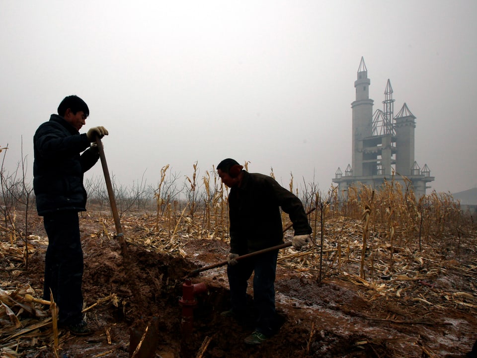 Zwei Männer arbeiten auf abgebranntem Feld, im Hintergrund Ruine eines Schlosses.