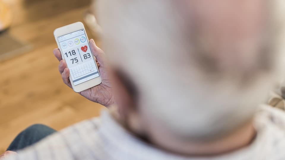 Ein älterer Mann liest auf dem Smartphone seine Blutdruckdaten ab.