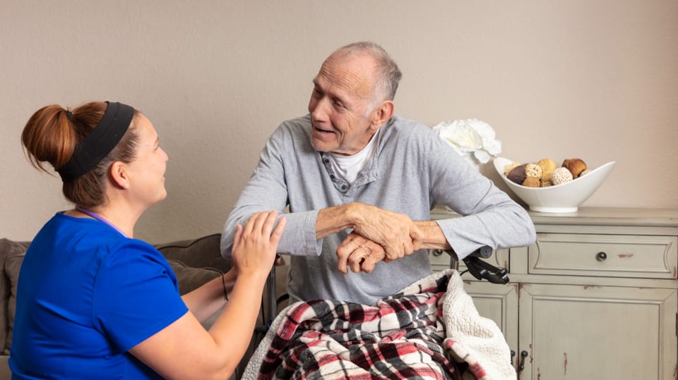 Eine Mitarbeiterin eines Hospizes spricht mit einem alten Mann im Rollstuhl