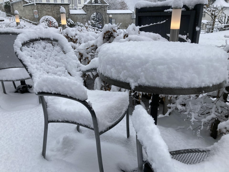 Schneebedeckte Stühle und ein Gartentisch.