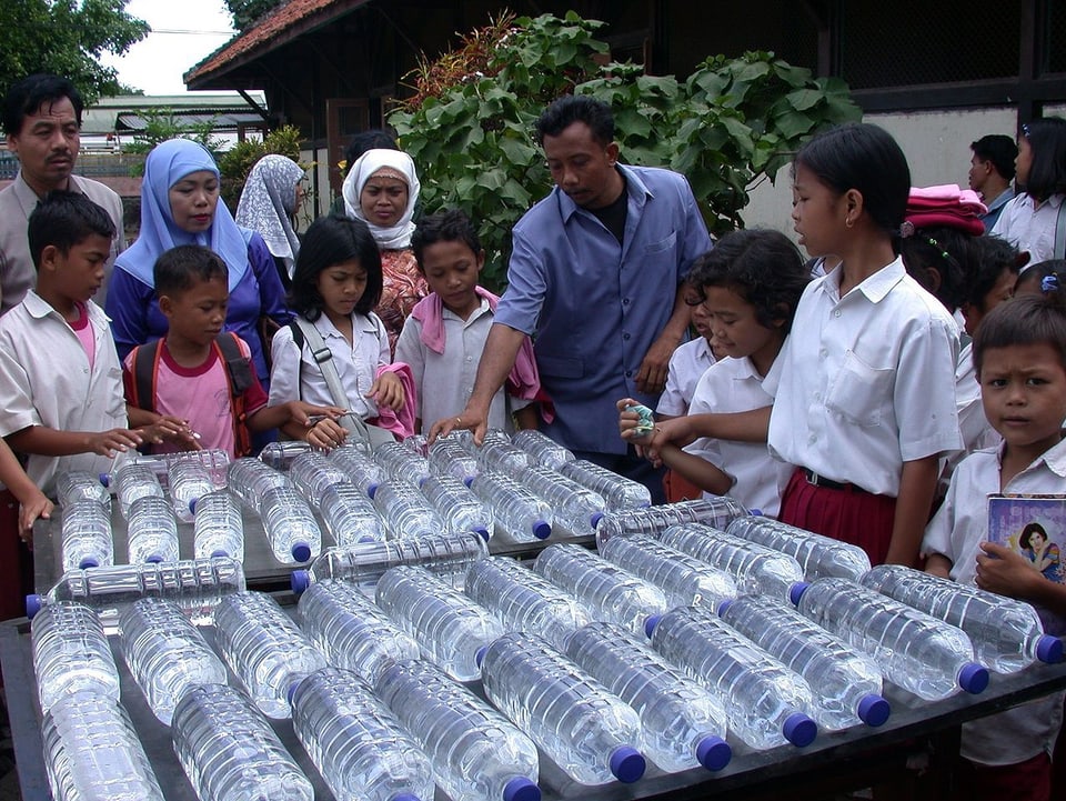 Kinder in Indonesien stehen um einen Tisch mit Wasserflaschen herum.
