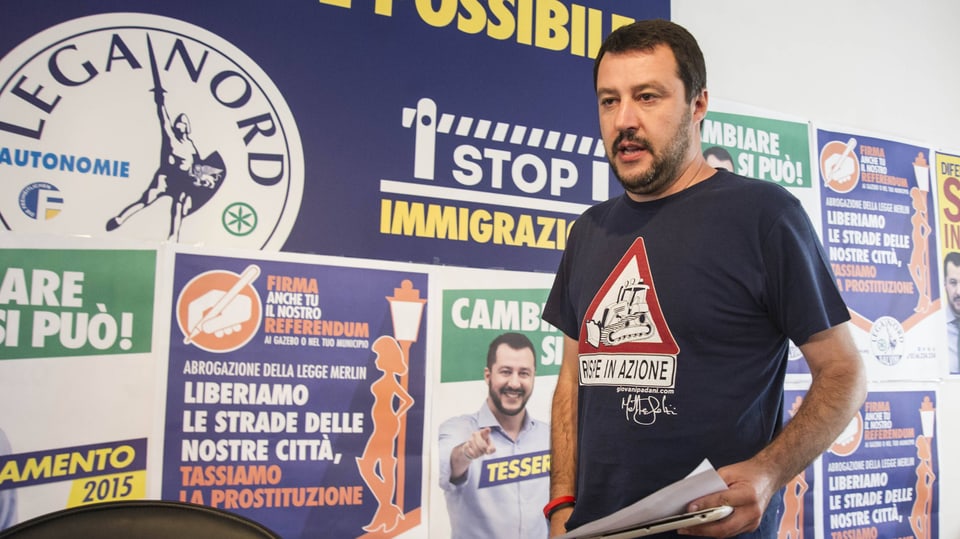 Salviini, ein Mann mit schwarzem Bart, steht vor Wahlplakaten seiner Partei.