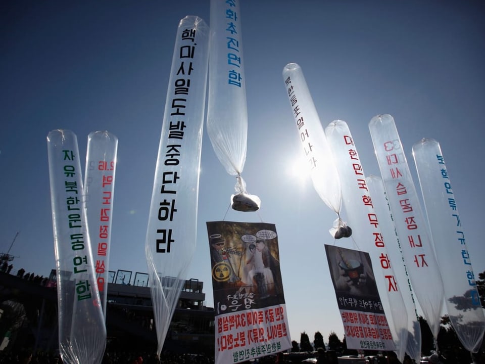 Protest balloons with banners against blue sky.