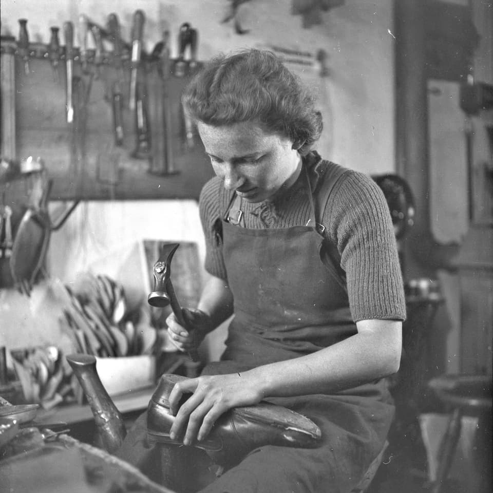 Eine Frau in ihrer Werkstatt, einen Halbschuh mit dem Hammer bearbeitend.
