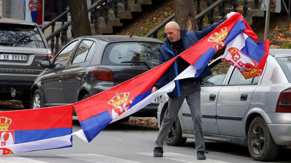 Ein Mann hält als Zeichen des Protests serbische Flaggen in die Höhe.
