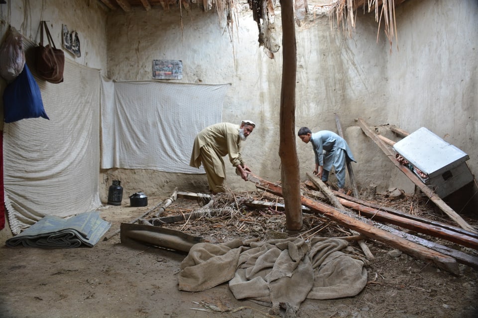 Ein älterer Mann und ein Junge räumen das Innere eines verwüsteten Hauses auf. 