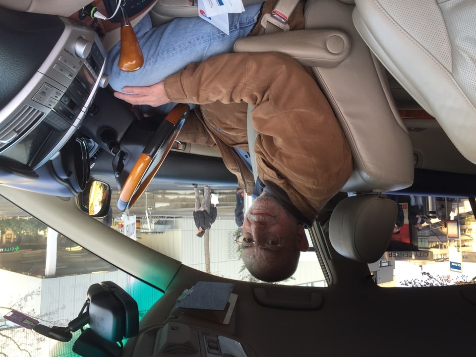 Der Taxichauffeuer Hans Herzig mit brauner Lederjacke sitzt am Steuer seines Autos.