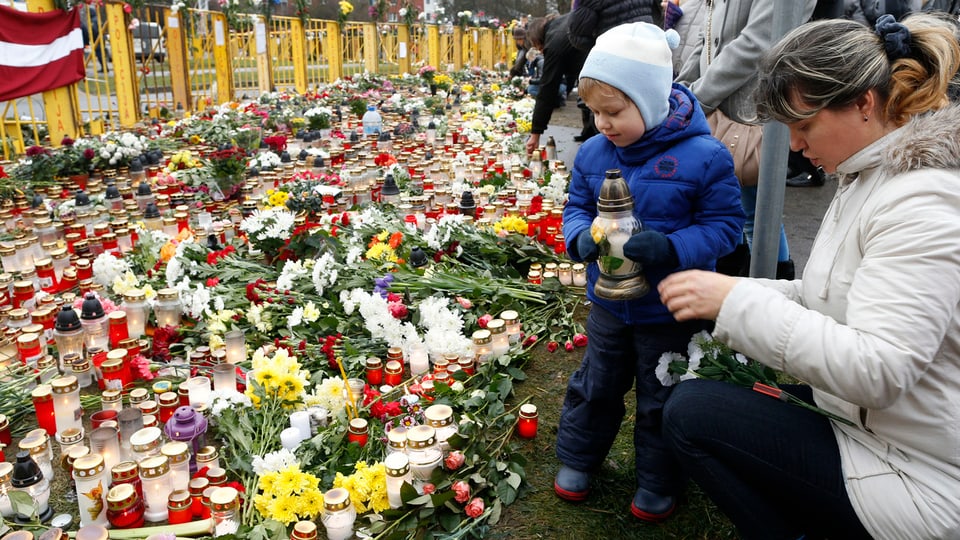 Ein Junge und dess Mutter legen Blumen und Kerzen am Unglücksort in Riga nieder. 
