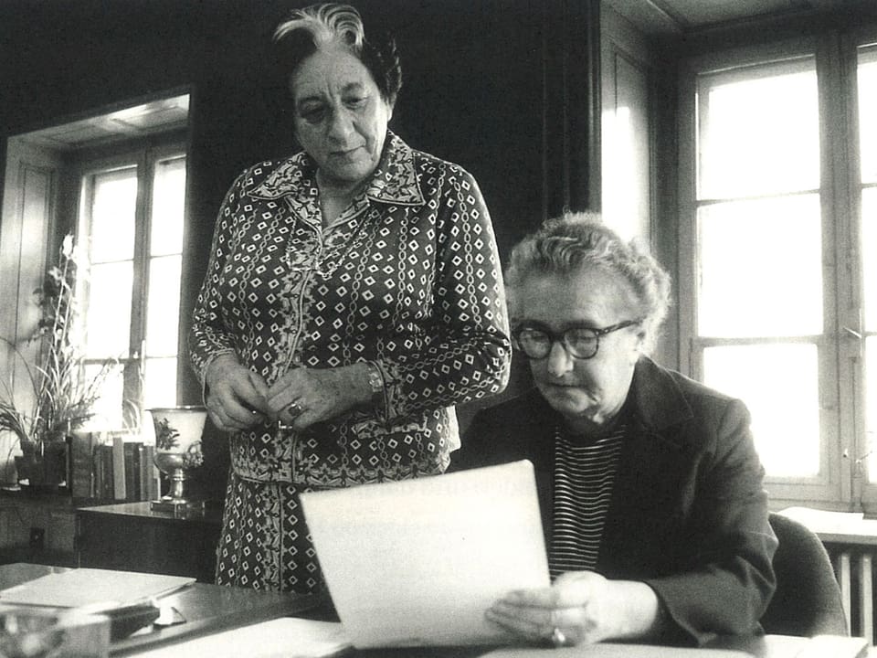 Marguerite Steiger und Hermine Raths arbeiten mit Akten an einem Schreibtisch.