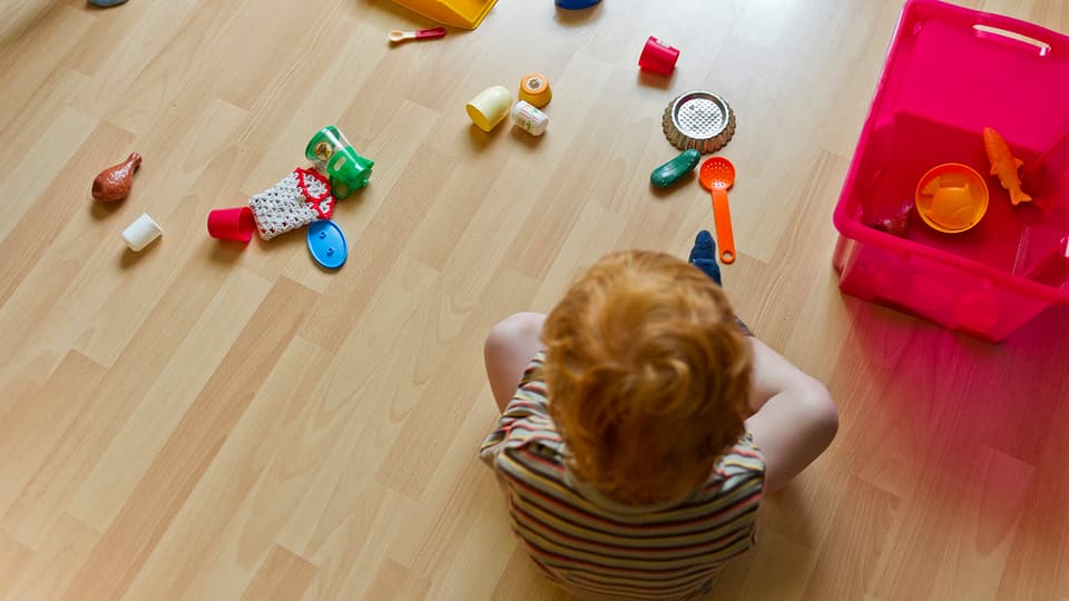 Kind sitzt am Boden mit Spielsachen.