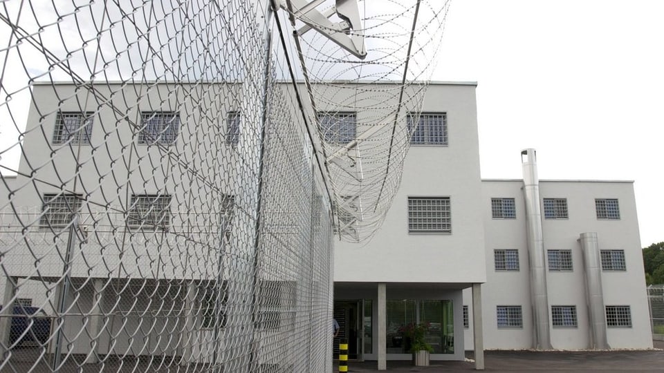 Gefängnisbau Bässlergut, weisses Haus mit Stacheldraht. 