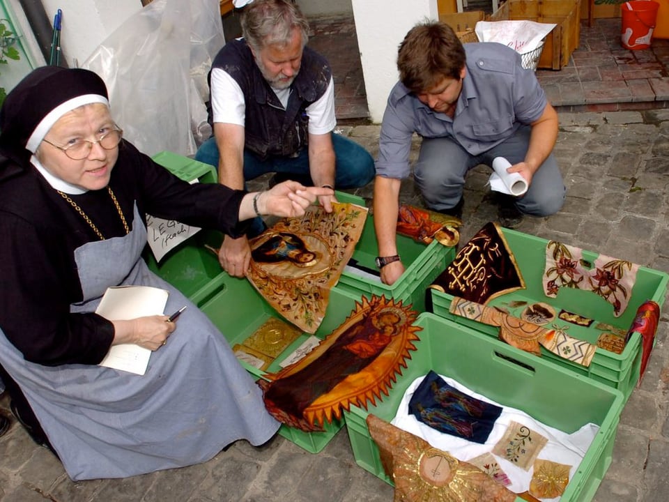 Eine Klosterfrau und zwei Helfer knien über den Kulturgütern.
