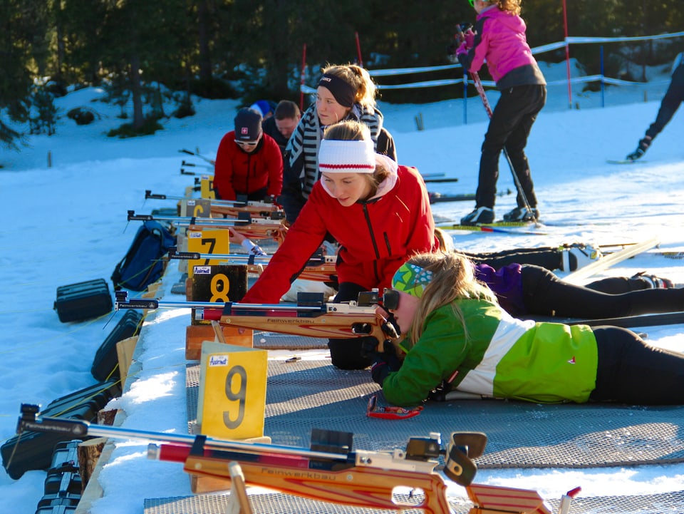 Jugendliche üben sich im Biathlon. Sie liegen auf dem Bauch im Schnee und schiessen.